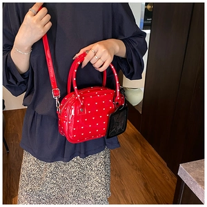 Dettaglio borsa in pelle verniciata rossa con cuori bianchi e ciondolo a cuore
