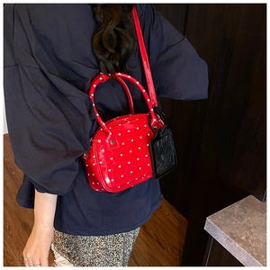 Detail of red glossy crossbody bag with white heart patterns worn by a model