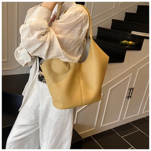 Detail of yellow lychee grain leather tote bag with round hanging ornament accessory