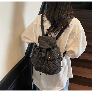 Detailansicht eines dunkelbraun karierten Rucksacks mit Schnallenverschluss und Kordelzug