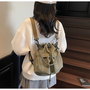Detailed view of an olive green drawstring bucket bag worn by a model on wooden stairs