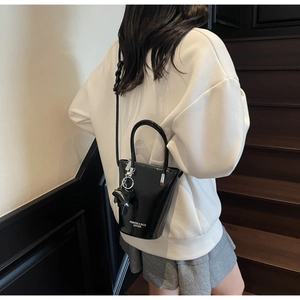 Detail of black glossy bucket bag with bear charm and logo strap on wooden background