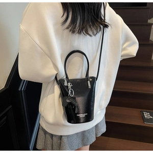 Detail of a black leather bucket bag with white logo and elephant charm on a model
