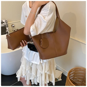 Detail of dark brown lychee texture leather tote bag with matching zippered pouch and charm