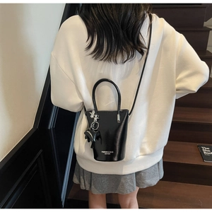 Detail of a black bucket bag with horse charm on a model in a minimalist stairway setting