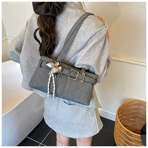 Detail of grey canvas bucket bag with silver bow charm and buckle accent shown on shoulder