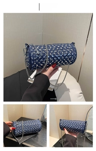 Detail of dark blue denim cylinder bag with silver studs and metal chain strap