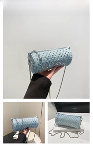 Detail of light blue denim cylinder bag with silver metal studs and thin chain strap