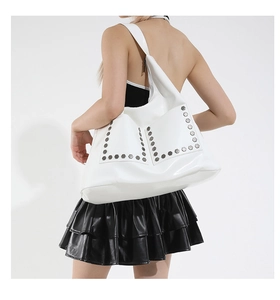 Detail of silver hexagonal rivets on white faux leather tote bag worn by a model