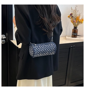 Deep blue cylindrical crossbody bag with silver studs on a stylish model outfit