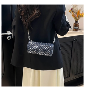 Detail of blue denim cylindrical crossbody bag with silver studs and chain strap