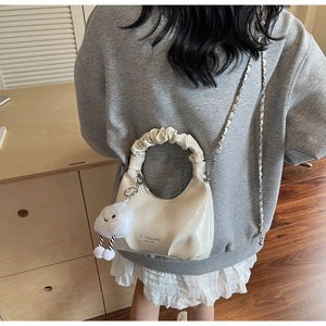 Detail of cream cloud bag featuring pleated handles and a cute plush charm accessory