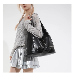 Detail view of a black studded tote bag worn on shoulder showing large capacity and hobo style