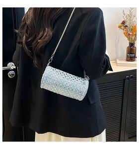 Detail of light blue denim barrel bag with silver studs and chain strap shown on shoulder