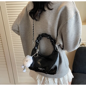 Detail of black glossy patent leather shoulder bag with ruffled handle and chain strap