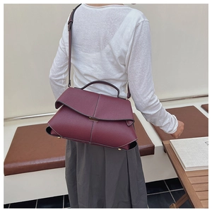 Detail of burgundy leather shoulder bag with white stitching and textured finish