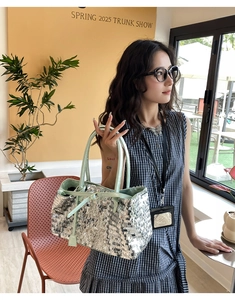Close-up of silver sequin tote bag with mint green leather handles held by a model
