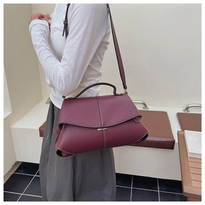 Detail of burgundy leather handbag with metal accent and adjustable shoulder strap