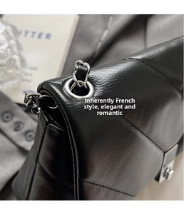 Detail of silver chain strap on black quilted leather crossbody bag with metal eyelets
