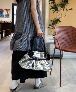 Detail shot of a silver sequined tote bag featuring black leather handles and metal buckle