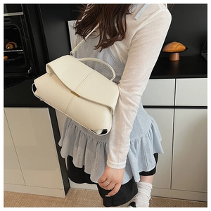 Close-up of cream textured leather crossbody bag styled with casual outfit in kitchen