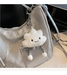 Close-up of white plush cloud charm with a smiley face on a silver metallic tote bag