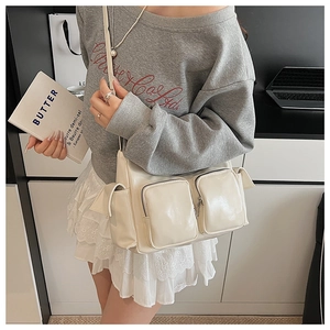 Detail of cream multi-pocket shoulder bag featuring glossy faux leather and utility style