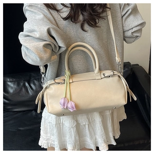 Close-up of creamy white baguette bag with lilac tulip pendant and lychee leather texture