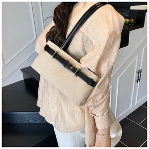 Détail du tissage beige et de la bandoulière en cuir noir avec boucles sur le sac baguette