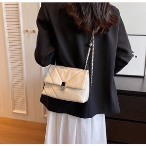 Détail du sac bandoulière matelassé crème avec chaîne et élément décoratif en métal