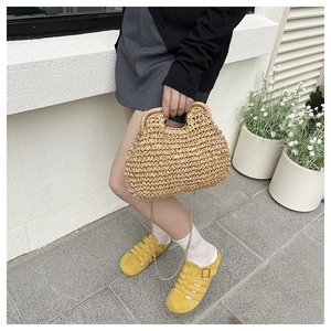 Detail of handwoven beige straw cloud bag with elegant gold chain strap in street setting