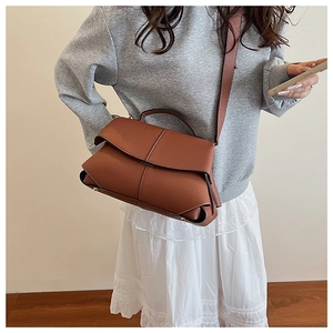 Detail of dark brown litchi leather bag with white contrast stitching and shoulder strap