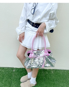 Close-up of a silver sequin tote bag with pink handles and lining on a model