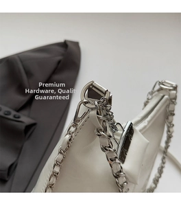 Detail van de zilveren ketting en metalen D-ring op een witte lederen schoudertas