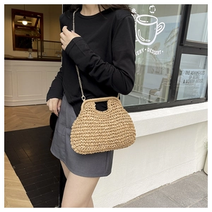 Detail of hand-woven straw handbag with gold chain strap shown in a street lifestyle setting