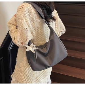 Detail of dark gray slouchy dumpling bag with silver star charm on wooden stairs