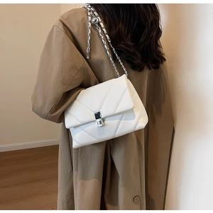 Detail of white quilted handbag with silver chain strap worn over a khaki trench coat