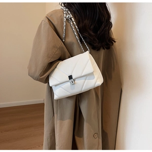 Nahaufnahme der weißen Stepptasche mit Kette über einem stilvollen Trenchcoat
