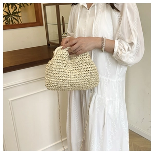 Detail of hand-woven beige straw handbag with gold chain strap held by a model