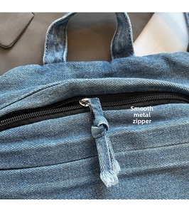 Detail of metal zipper and denim pull cord on blue washed denim crossbody bag