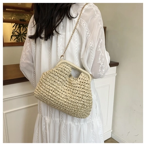 Detail of hand-woven beige straw bag with gold chain strap on white lace dress