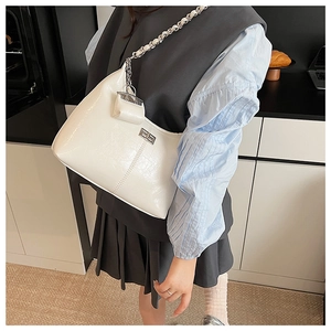 Detail van witte lakschoudertas met zilveren ketting en een mini tas-accessoire eraan