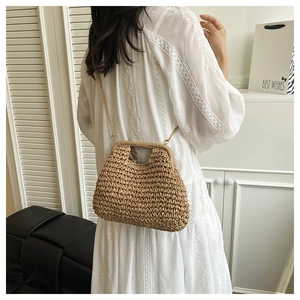 Détail d'un sac bandoulière en paille tressée avec chaîne dorée sur une robe d'été