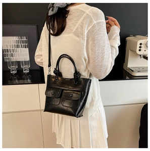 Detail of black faux crocodile skin handbag with dual front pockets and top handle strap