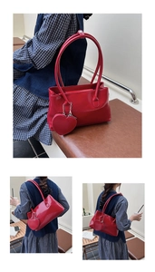 Detail of red leather baguette bag featuring a glossy finish and a cute heart charm