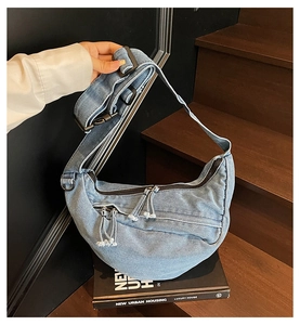 Detail of light blue denim hobo bag featuring metal zippers and adjustable shoulder strap