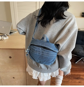 Detail of blue denim crossbody bag showing washed fabric texture and black zipper