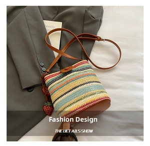 Detail showing colorful striped woven bucket bag with leather strap and strawberry charm