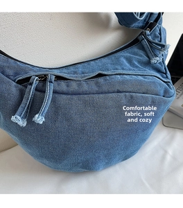 Detail of blue denim crescent bag showing double zippers and washed fabric texture