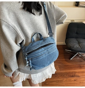 Detail view of washed blue denim crossbody bag featuring a wide strap and front zipper pocket